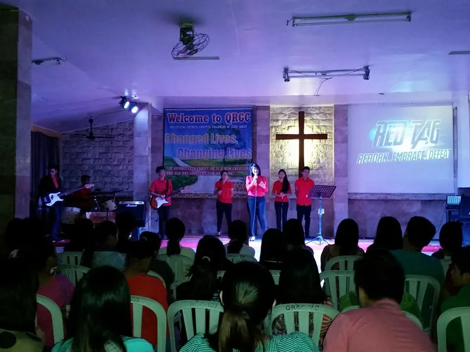 The Red Tag event at Quest Molino, a worship team on a small stage in front of a seated crowd
